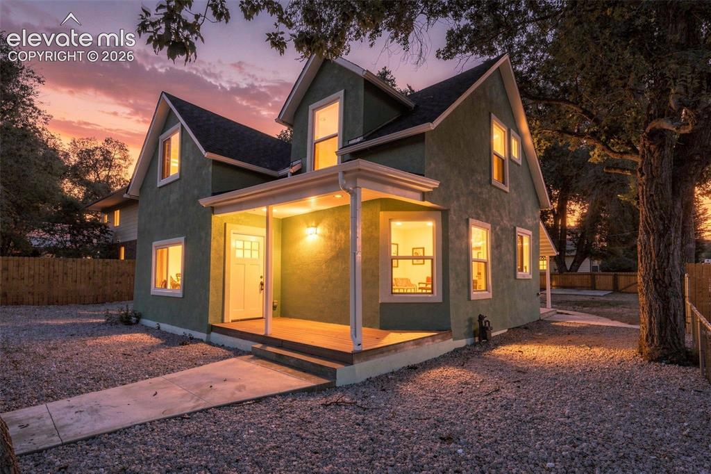 Image 1 of 50: Green stucco exterior with white trim, covered front porch, gravel landscap