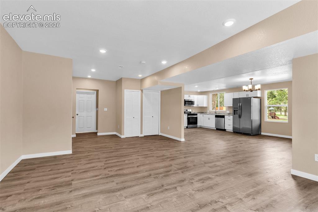 Image 13 of 50: Spacious interior with wood-finish flooring, recessed lighting, and a kitch