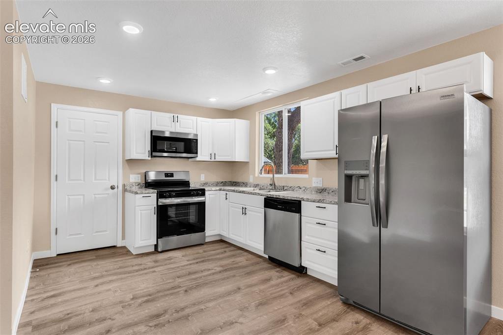 Image 16 of 50: Kitchen featuring white cabinetry, stainless steel appliances, speckled cou