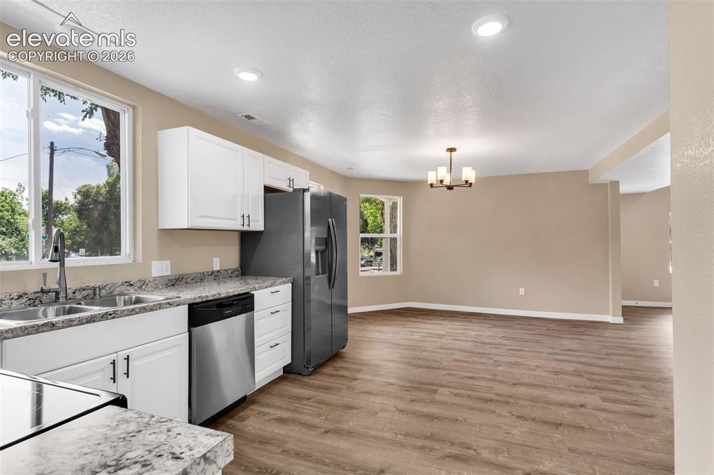 Image 18 of 50: Kitchen and living area featuring wood-finish flooring, white cabinetry, st
