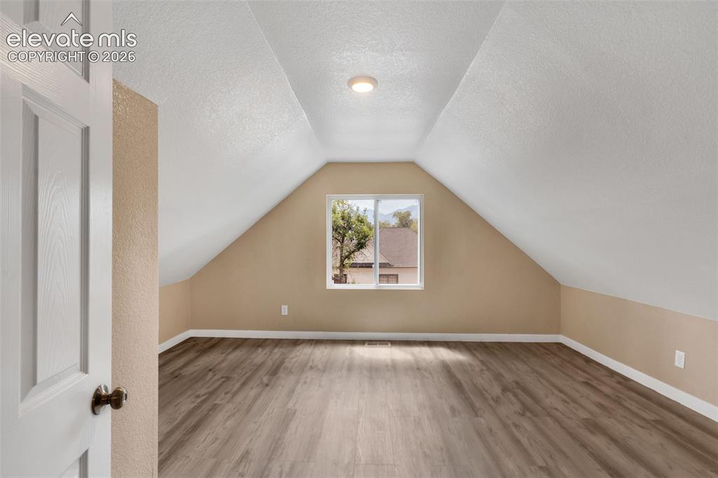 Image 33 of 50: Spacious room featuring vaulted ceilings, wood-finish flooring, a window, a