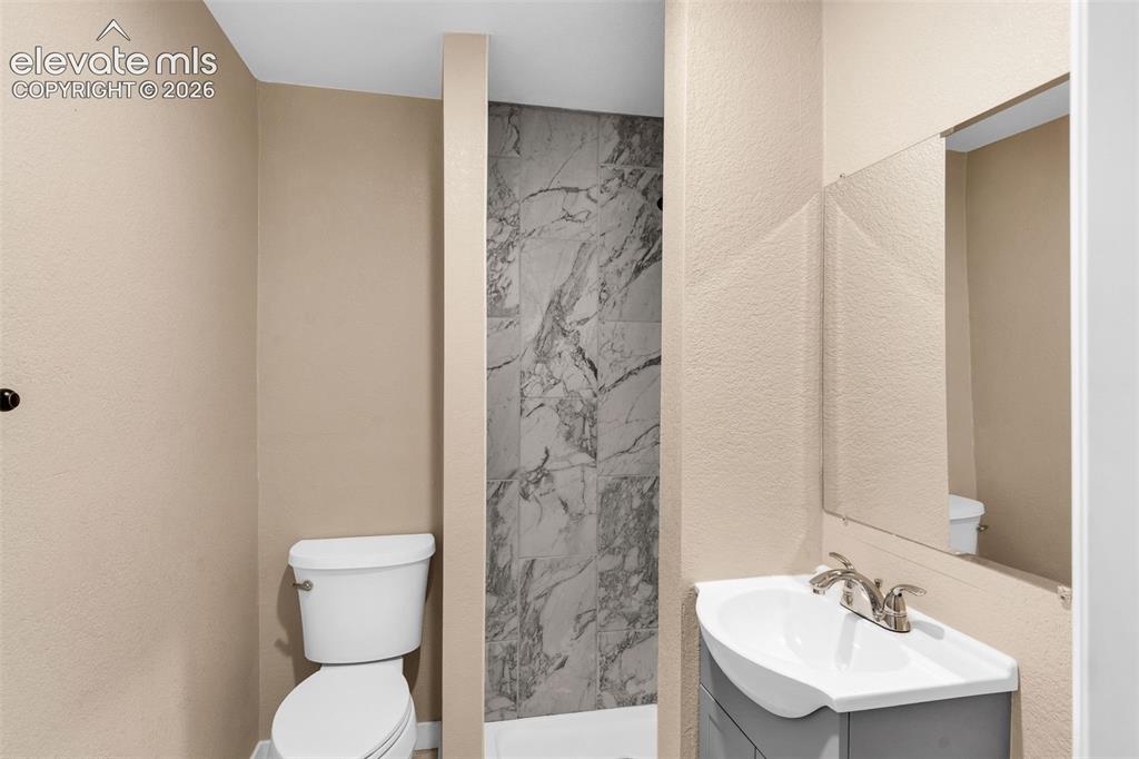 Image 36 of 50: Walk-in shower with large format marble-look tile, white toilet, and a vani