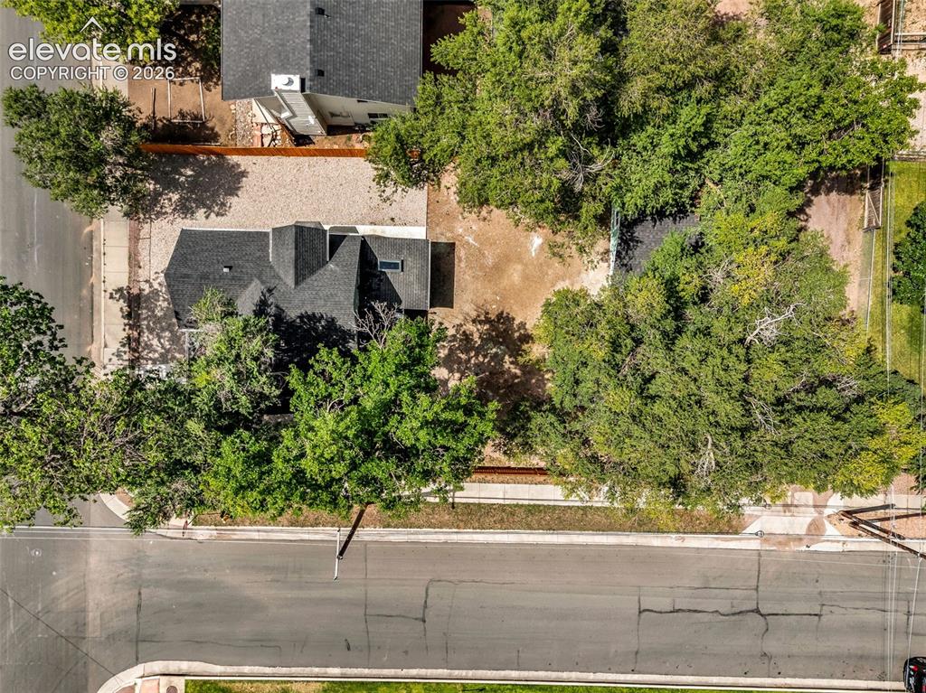 Image 45 of 50: Pitched roofline, mature trees, gravel landscaping, paved street frontage,