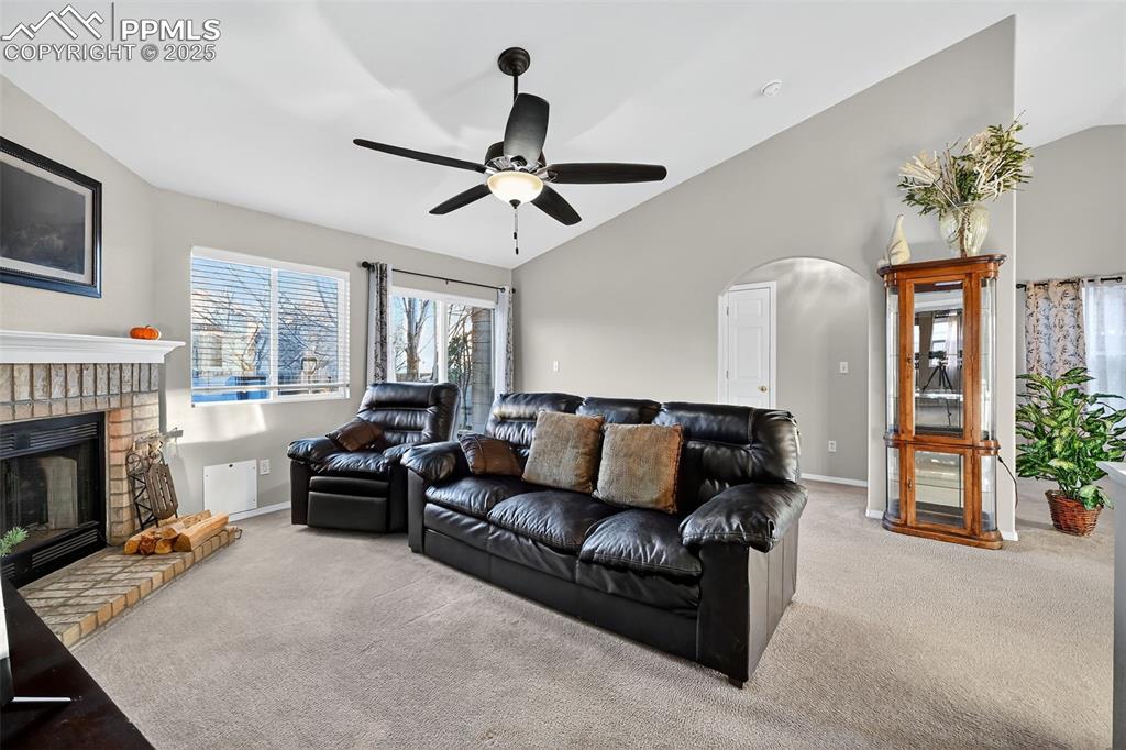 Image 11 of 41: Carpeted living room with lofted ceiling, a brick fireplace, arched walkway