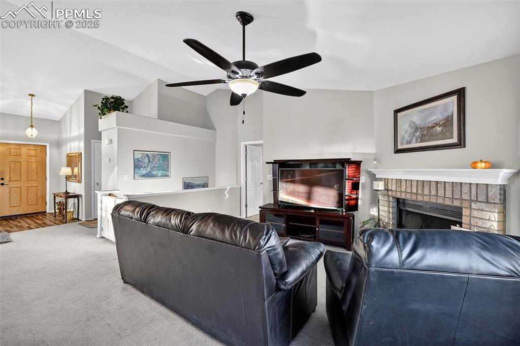 Image 12 of 41: Carpeted living area featuring a brick fireplace, a ceiling fan, and high v