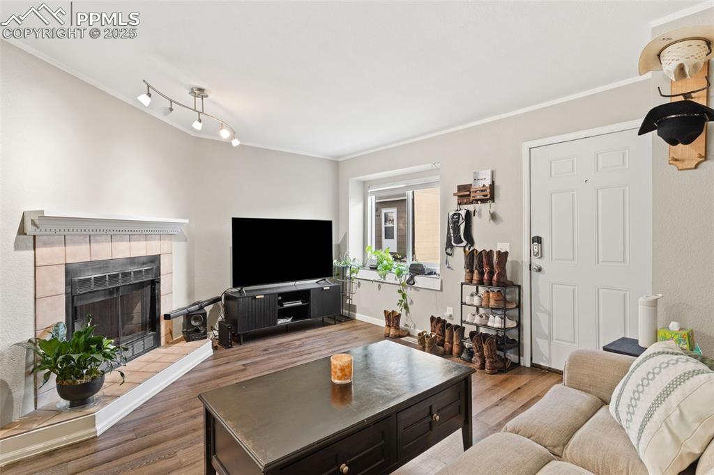 Image 7 of 26: Living room with a tile fireplace, ornamental molding, and wood finished fl