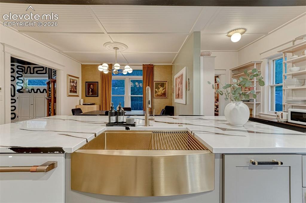 Image 24 of 50: White stone countertops with dark veining, gold-toned farmhouse sink, light
