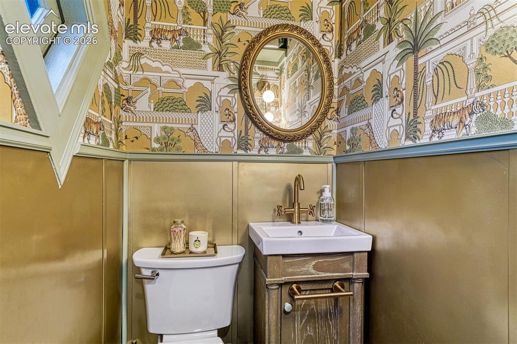 Image 32 of 50: Patterned wallpaper with an ornate gilded mirror, a white rectangular sink 