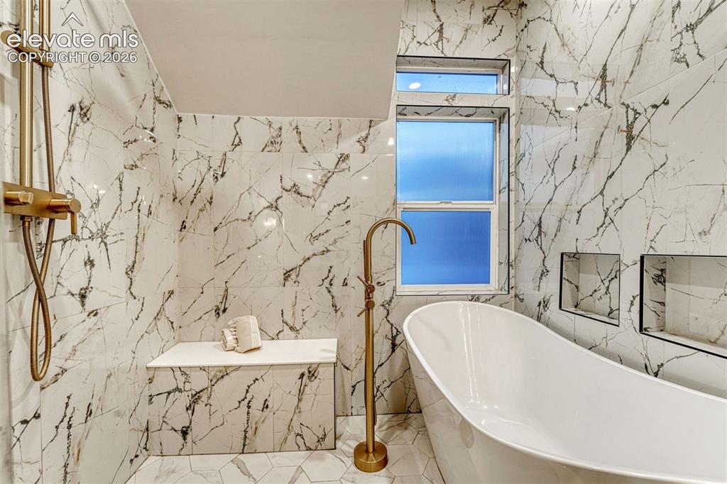 Image 43 of 50: Freestanding soaking tub with a floor-mounted gold-tone faucet, walk-in sho