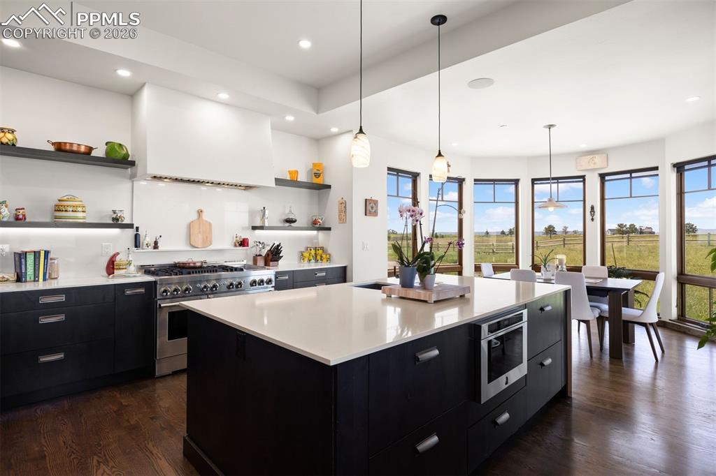 Image 19 of 39: JennAir gas range with custom hood, open shelving, and eat-in area surround