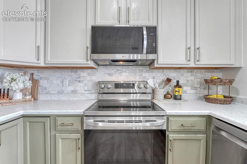 Image 20 of 50: Beautifully tiled backsplash, painted wood cabinets, and solid surface coun