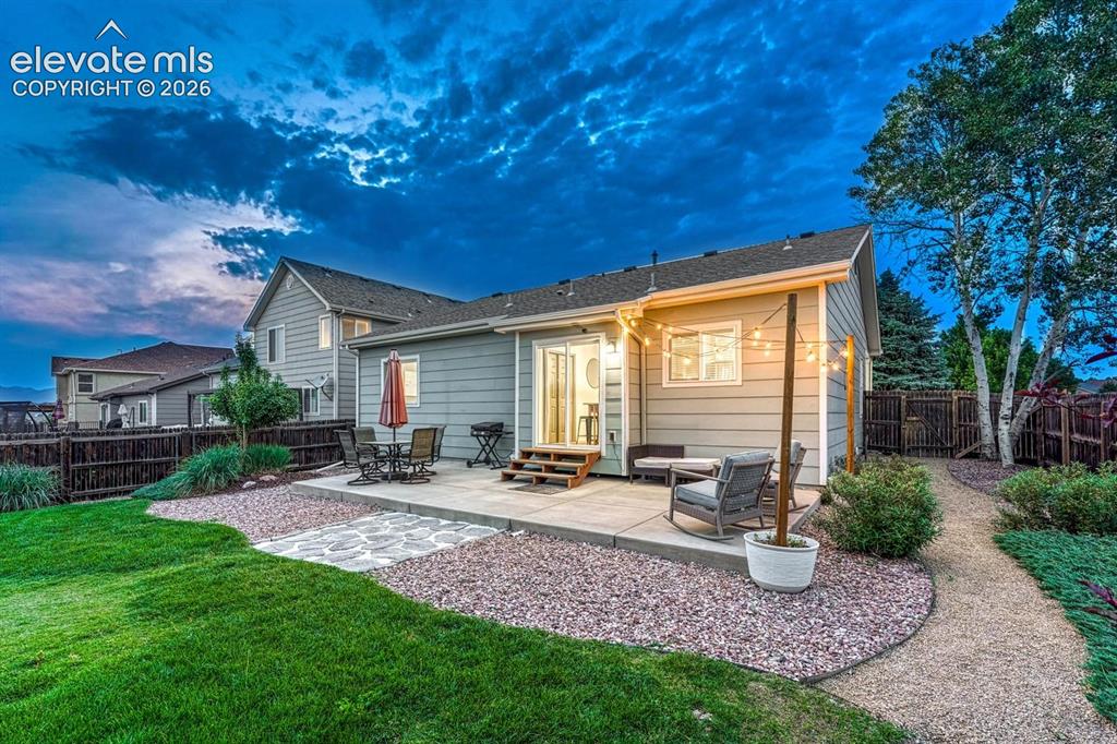 Image 42 of 50: Sunset view of the backyard patio and grass areas with trees and shrubs.