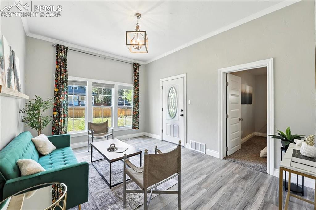 Image 7 of 36: Living area with a chandelier, wood finished floors, and crown molding