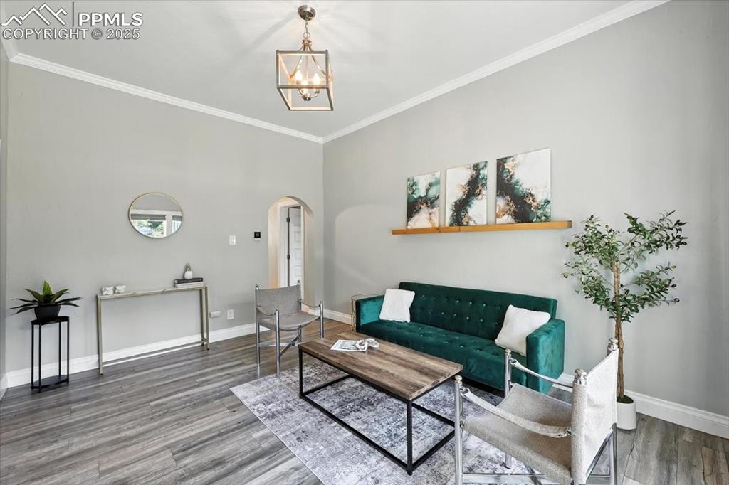 Image 8 of 36: Living area featuring arched walkways, a chandelier, crown molding, and woo