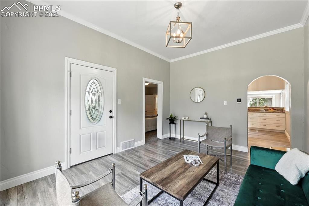 Image 9 of 36: Living room with wood finished floors, a chandelier, crown molding, and arc