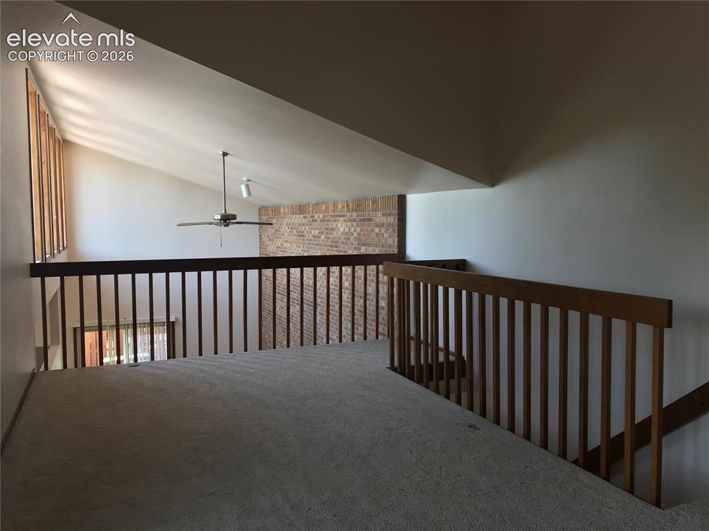 Image 23 of 35: Carpeted loft space with wood railing, vaulted ceilings, and a ceiling fan
