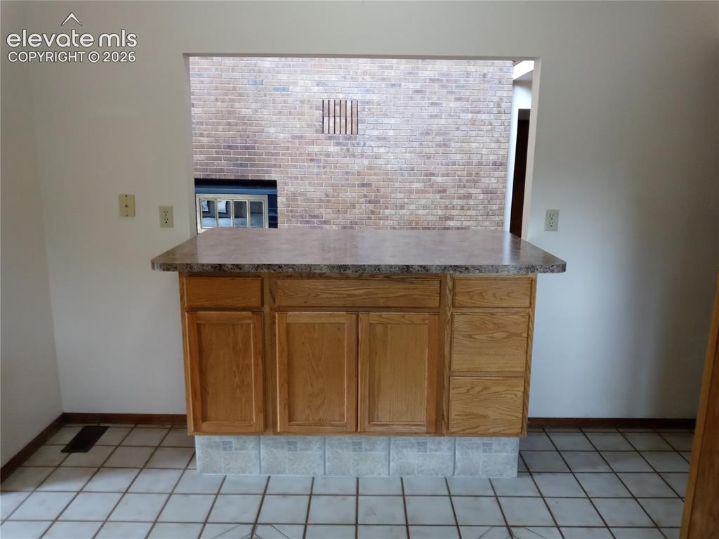 Image 5 of 35: Central kitchen island with wood-finish cabinetry and a speckled countertop