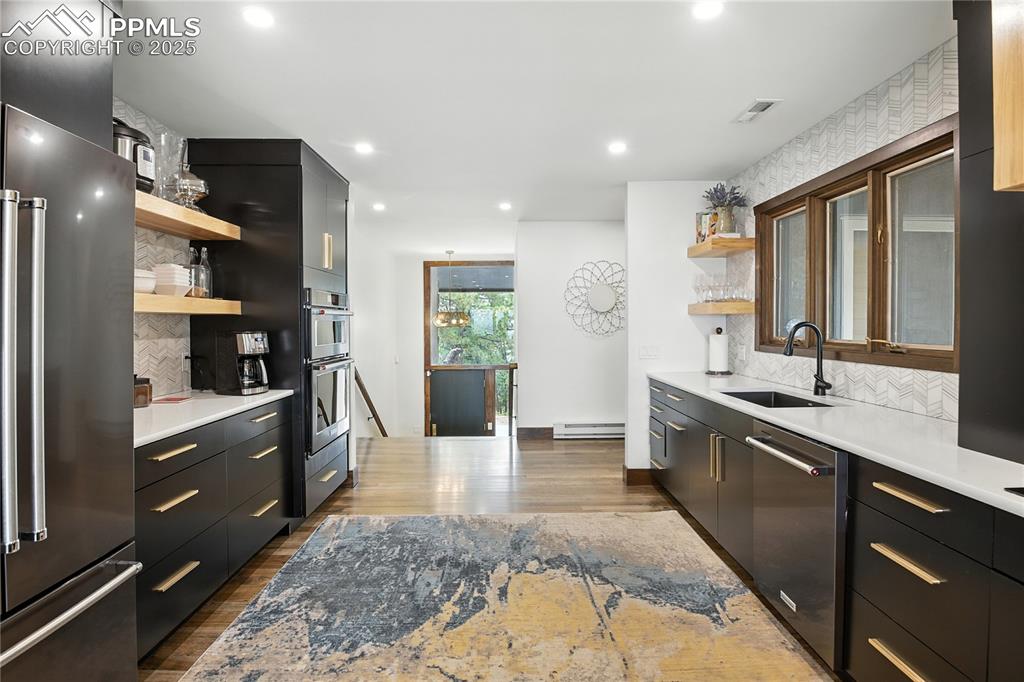Image 11 of 50: Kitchen featuring open shelves, backsplash, dark cabinets, appliances with 