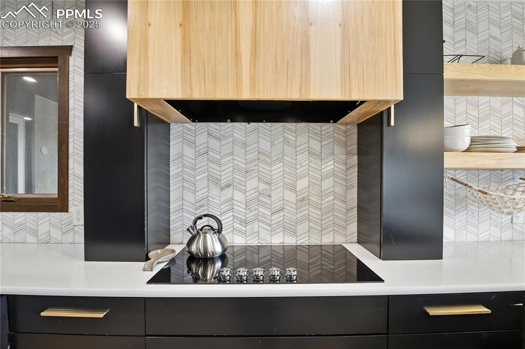 Image 14 of 50: Kitchen with premium range hood, black electric cooktop, dark cabinetry, li