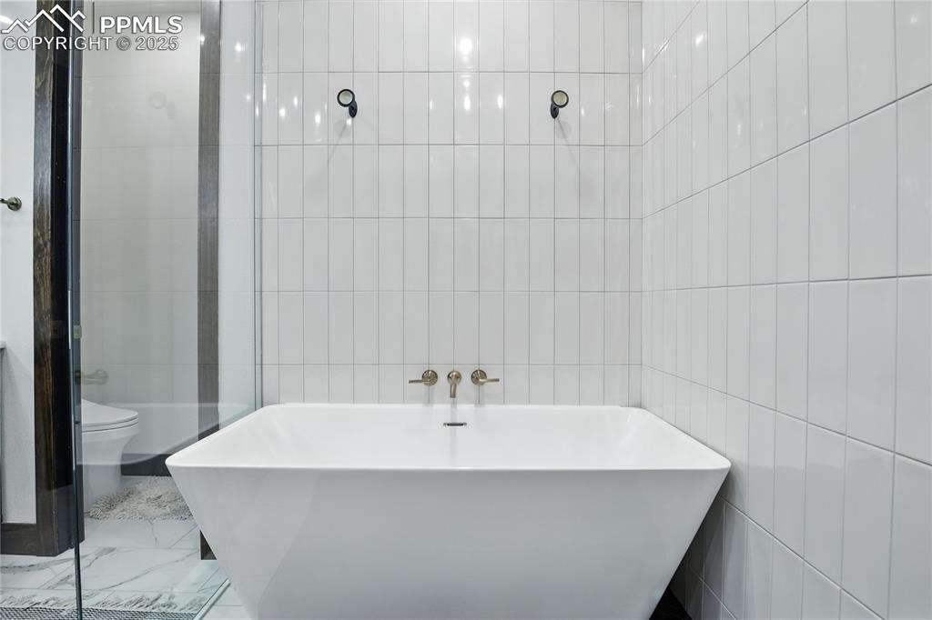 Image 28 of 50: Bathroom with a soaking tub, tile walls, marble finish flooring, and a tile