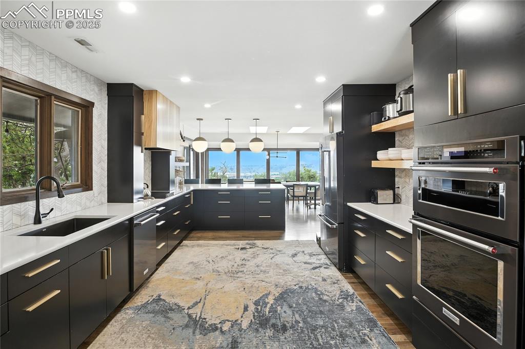 Image 4 of 50: Kitchen featuring dark cabinetry, modern cabinets, appliances with stainles