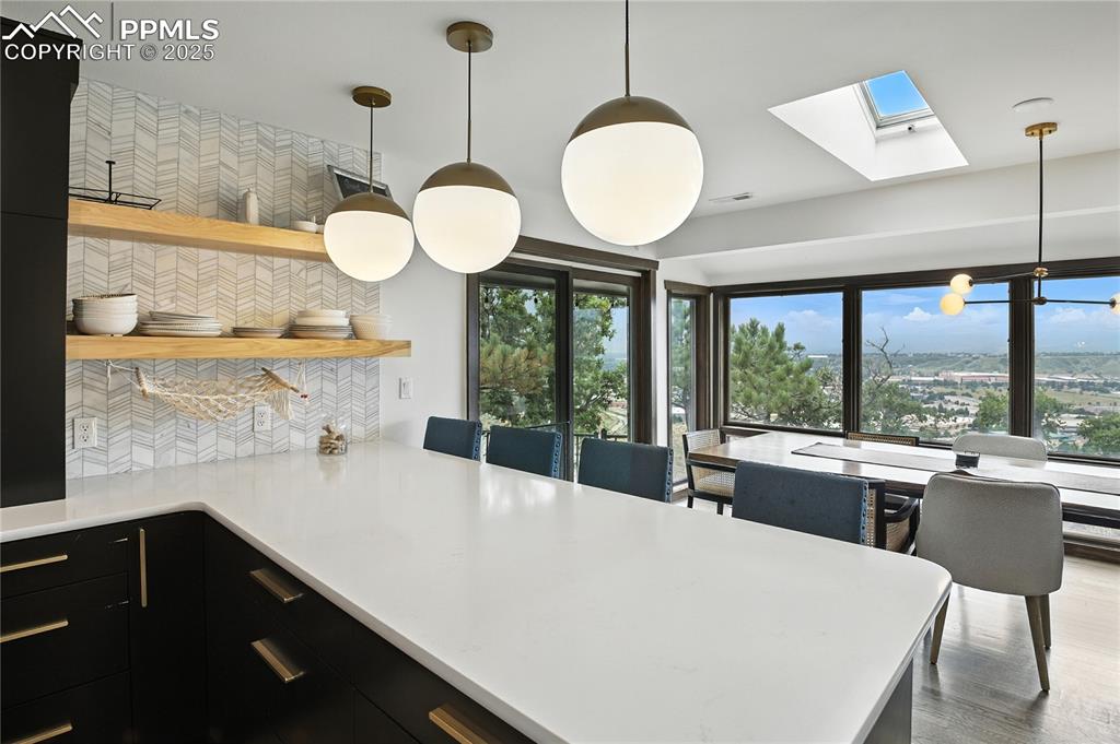 Image 9 of 50: Kitchen with hanging light fixtures, dark cabinets, tasteful backsplash, a 