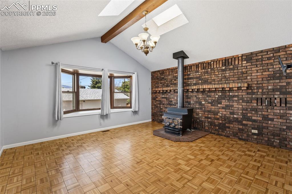 Image 14 of 50: Vaulted ceiling with exposed beam and skylights, featuring a brick accent w
