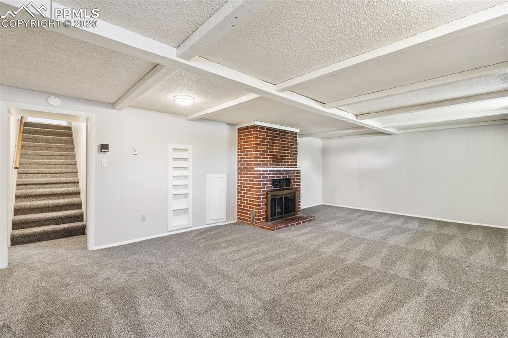 Image 30 of 50: Spacious room with a brick fireplace, built-in shelving, light gray carpeti