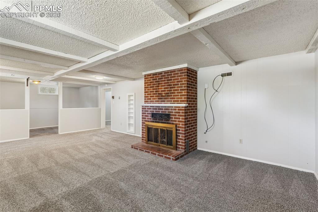 Image 32 of 50: Spacious carpeted room featuring a brick fireplace with a brass firebox, ex