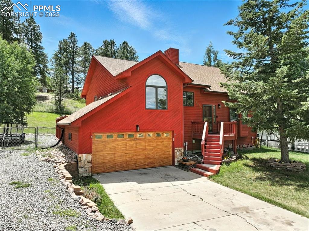 Caption: View of front of house with stone siding, an attached garage, concrete driveway, a chimney, and roof