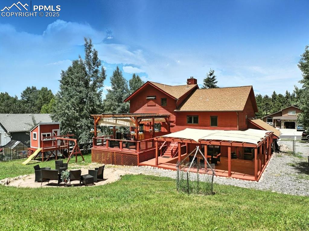 Image 32 of 36: Rear view of property featuring a wooden deck, a chimney, a playground, a l