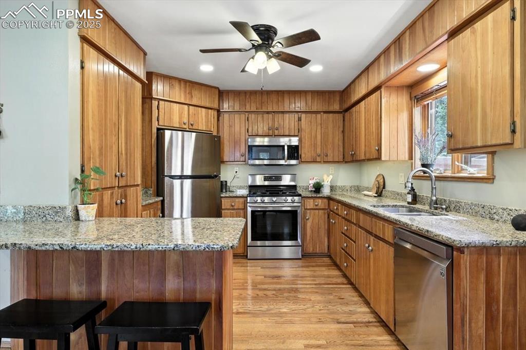 Image 8 of 36: Kitchen featuring stainless steel appliances, a peninsula, brown cabinetry,