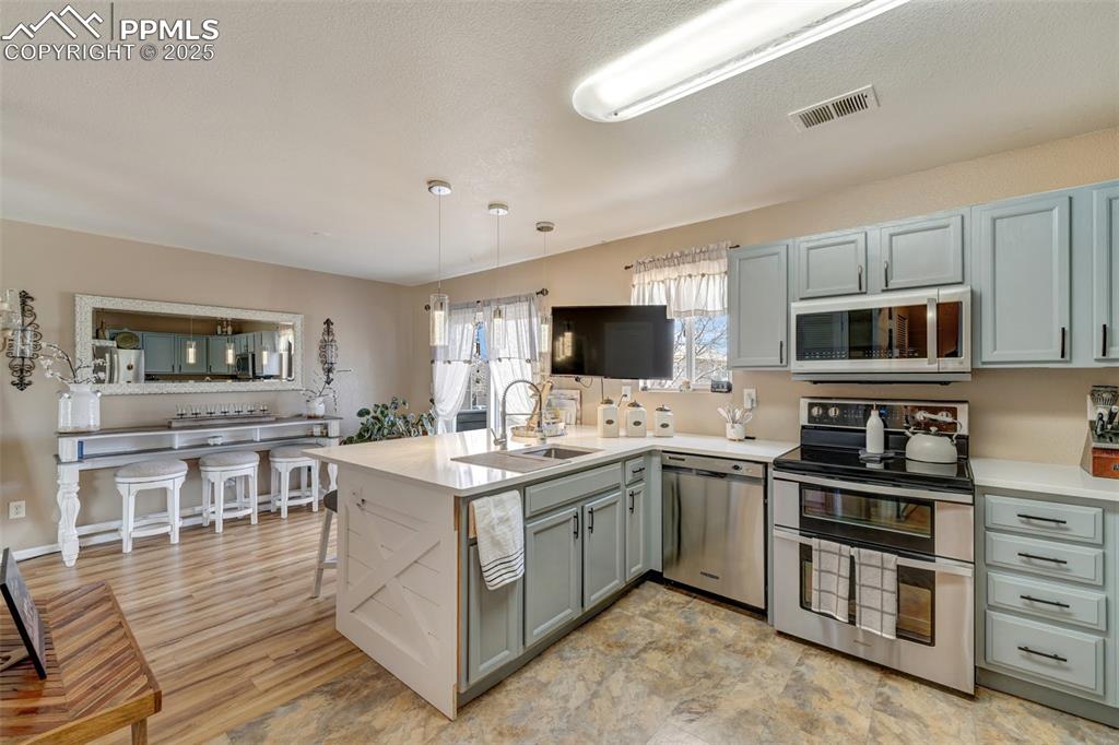 Image 9 of 23: Kitchen with visible vents, a sink, light countertops, appliances with stai