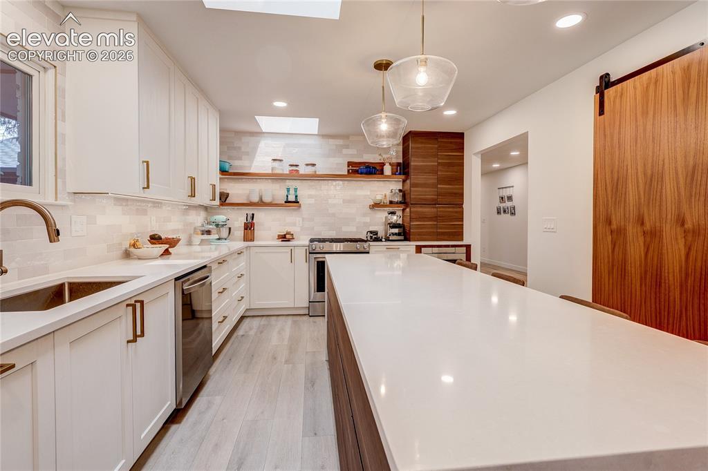 Image 11 of 50: Modern kitchen featuring white cabinetry, a large center island with a ligh