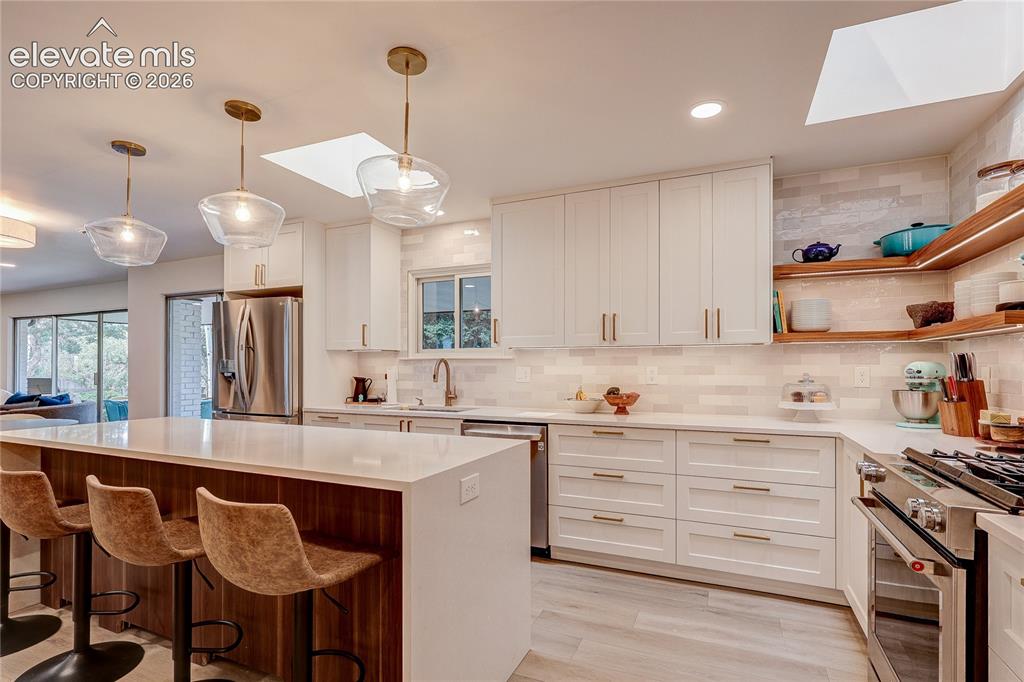 Image 12 of 50: Kitchen featuring a spacious island, white cabinetry, integrated stainless