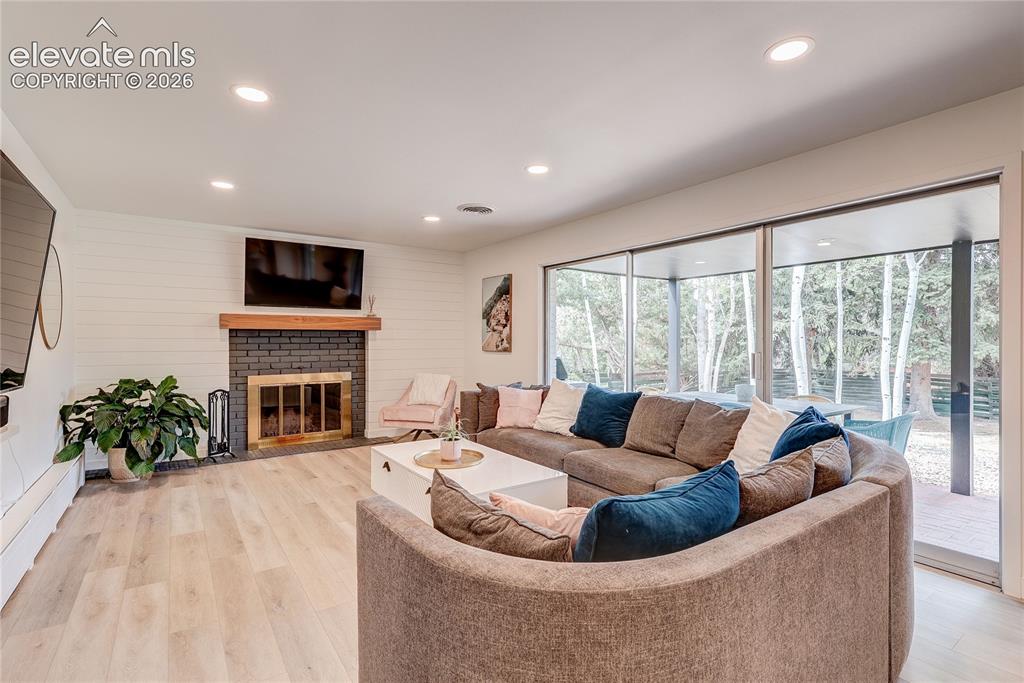 Image 21 of 50: Recessed lighting, wood-finish flooring, fireplace with dark brick surround