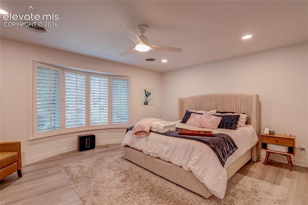 Image 33 of 50: Bay window with white plantation shutters, wood-finish flooring, ceiling fa