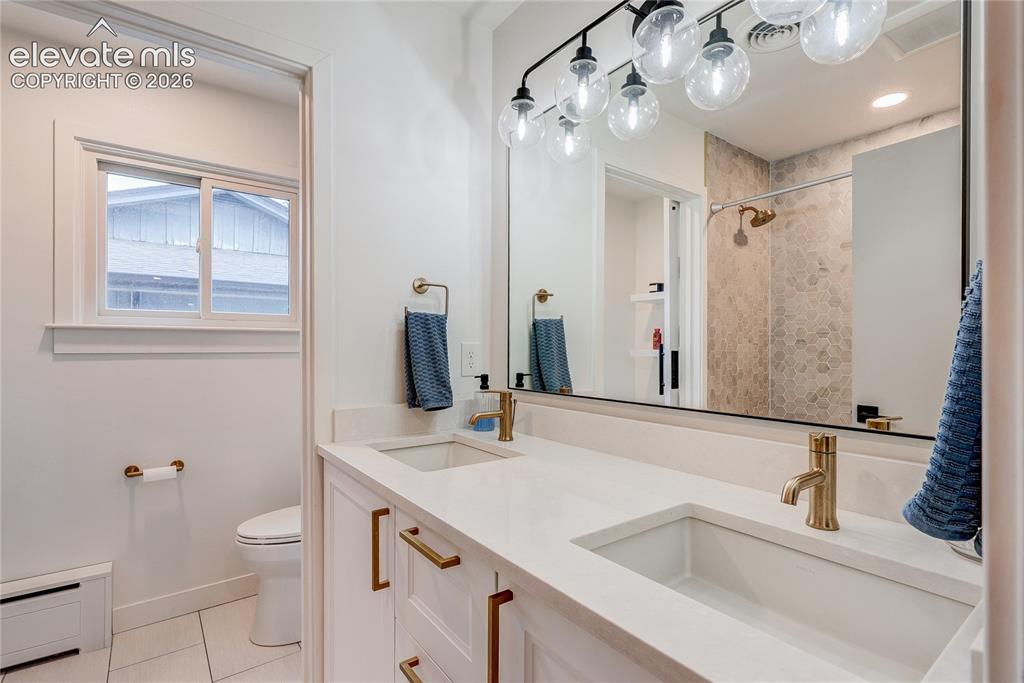 Image 35 of 50: Dual vanity with integrated sinks, brass-finish fixtures, and a large wall-
