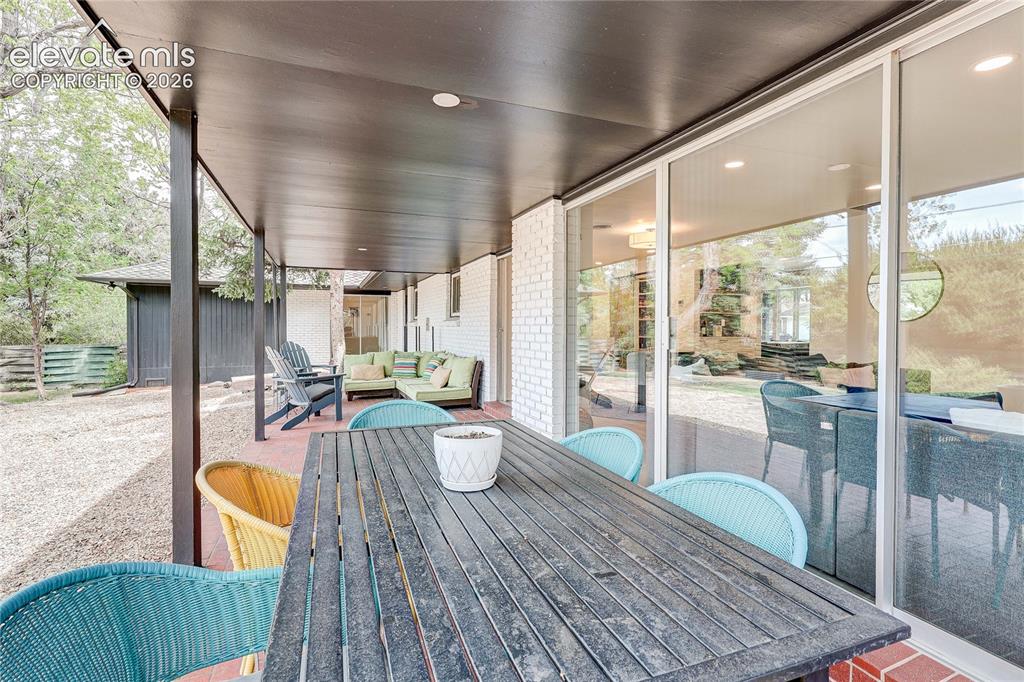 Image 40 of 50: Covered patio with brick flooring, recessed lighting, white brick exterior,