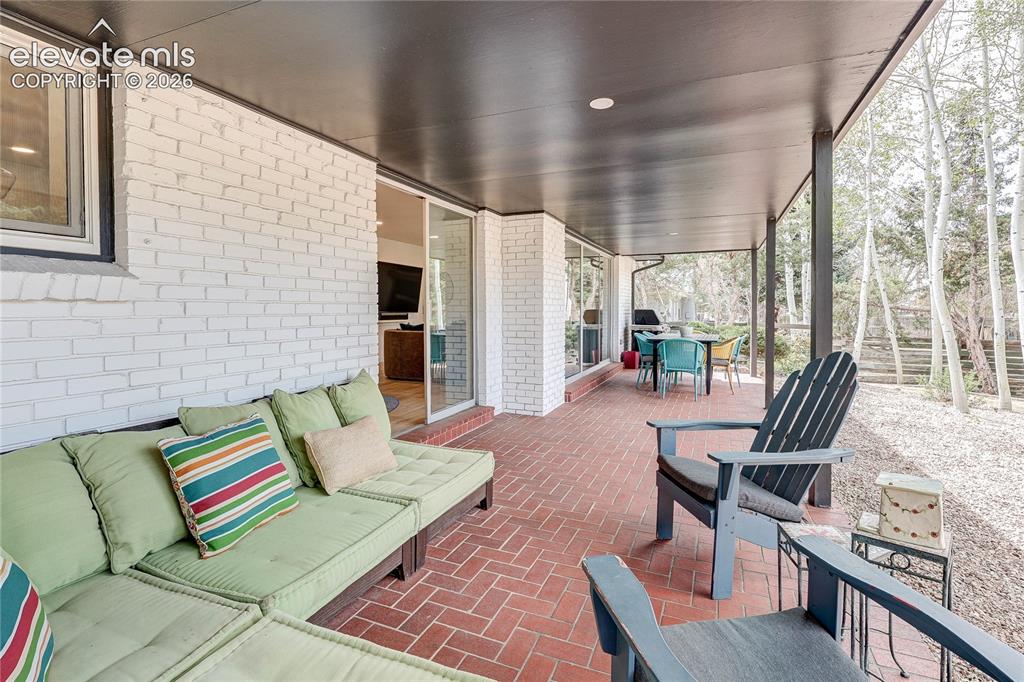Image 41 of 50: Covered patio featuring brick flooring and white painted brick exterior