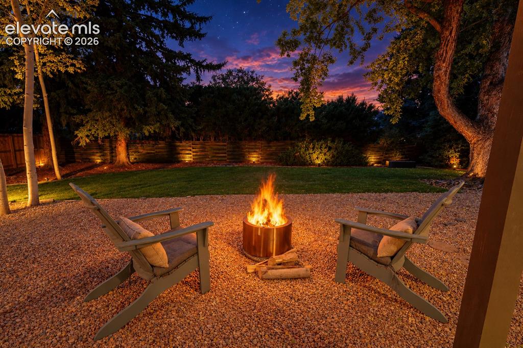 Image 42 of 50: Gravel patio featuring a fire pit, surrounded by a manicured lawn and matur