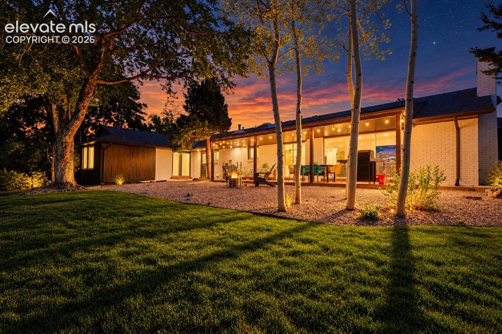 Image 45 of 50: Spacious outdoor patio with string lighting, expansive lawn, mature trees,
