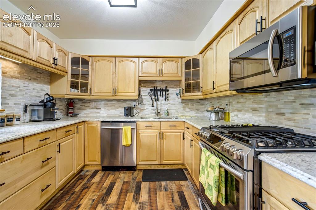 Image 15 of 50: Kitchen featuring light-tone cabinetry, a mosaic tile backsplash, and grani