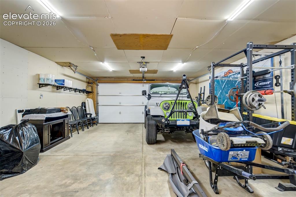 Image 42 of 50: Spacious garage featuring a white overhead door, concrete flooring, and amp