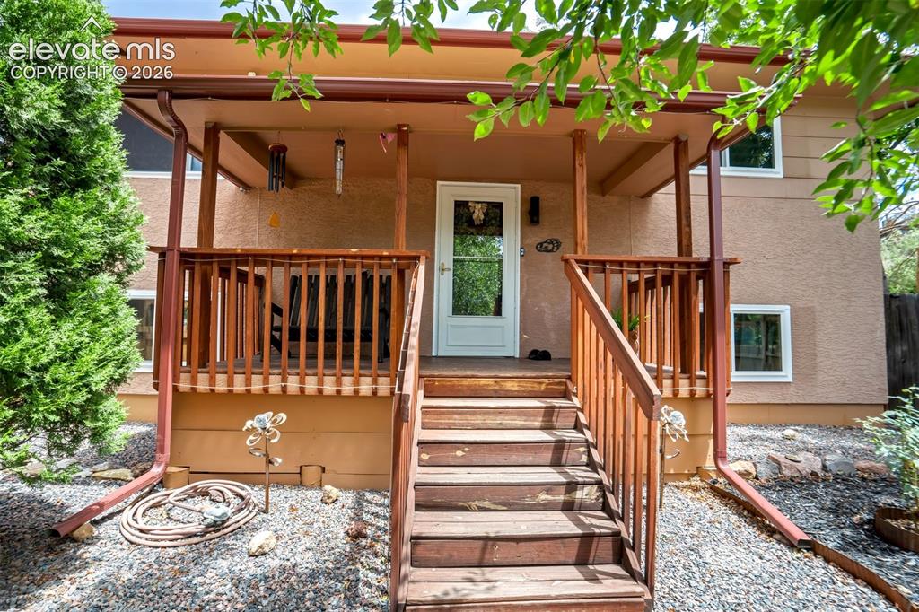 Image 8 of 50: Covered front porch with wood railings and stairs leading to a white glass-