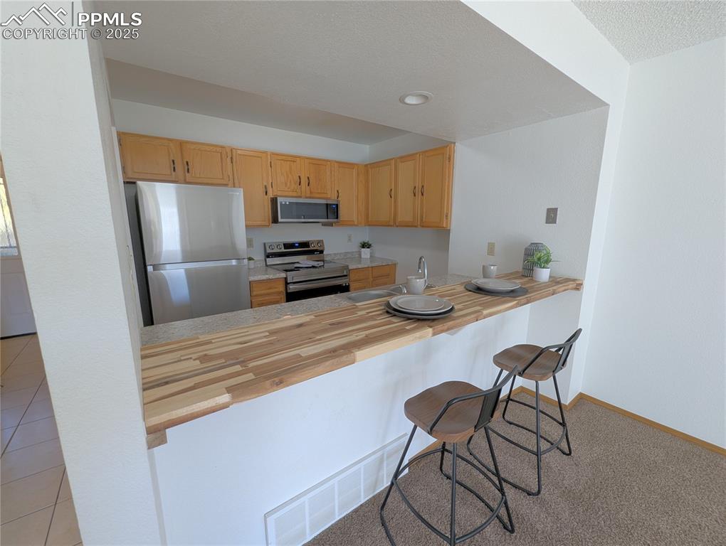 Image 3 of 19: Kitchen featuring stainless steel appliances, a breakfast bar wooden counte