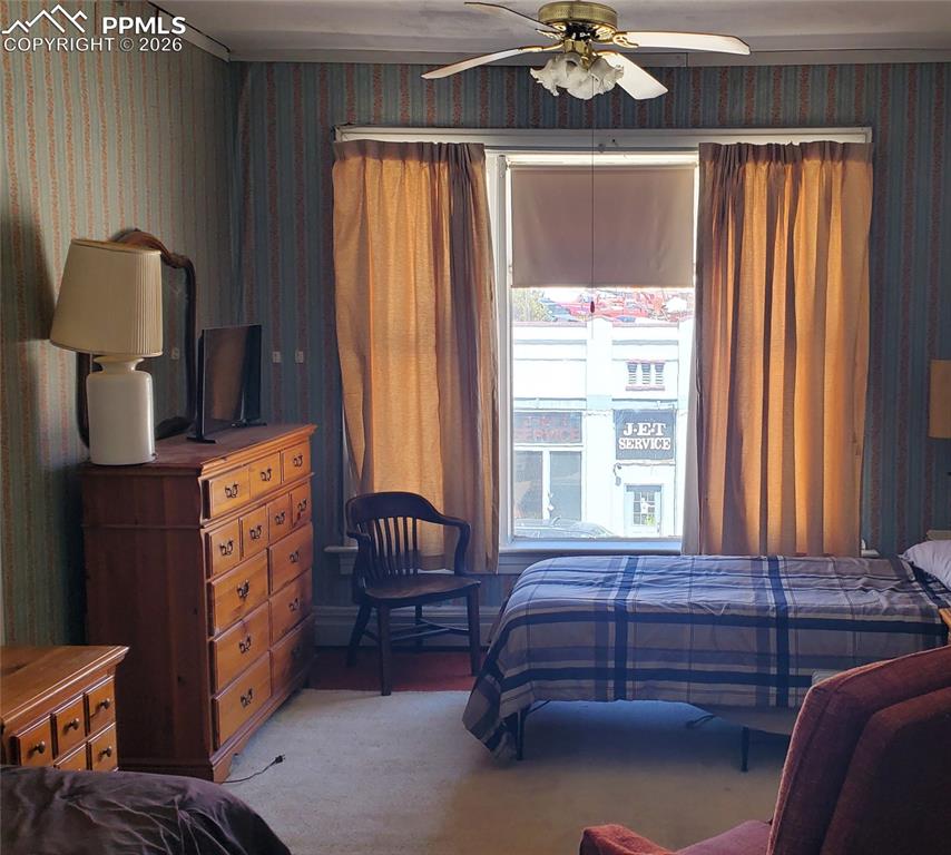Image 29 of 36: Bedroom with light colored carpet, ceiling fan, and wallpapered walls