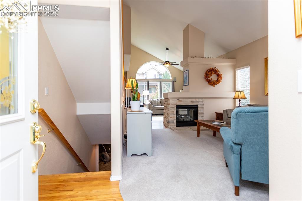 Image 13 of 47: Living area with lofted ceiling, a fireplace, a ceiling fan, light wood-sty