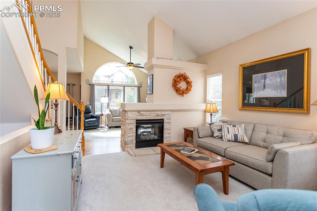 Image 5 of 47: Living room with stairs, a stone fireplace, healthy amount of natural light
