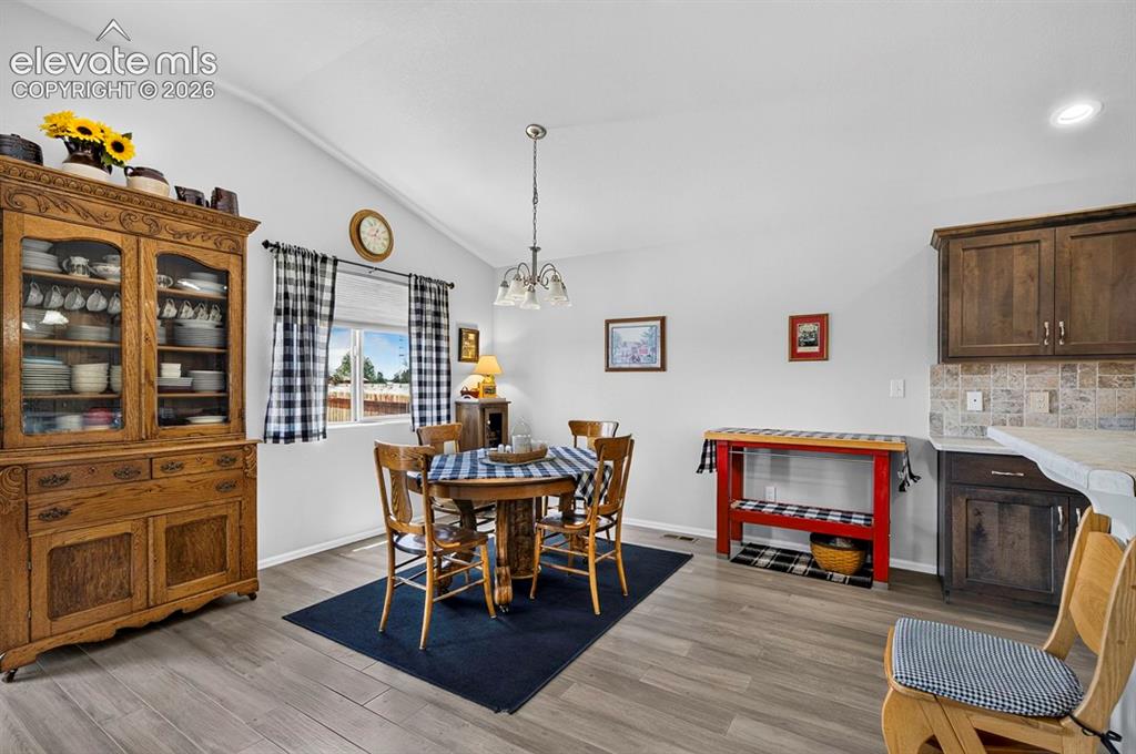 Image 11 of 40: Dining area featuring vaulted ceilings, wood-finish flooring, and a large w